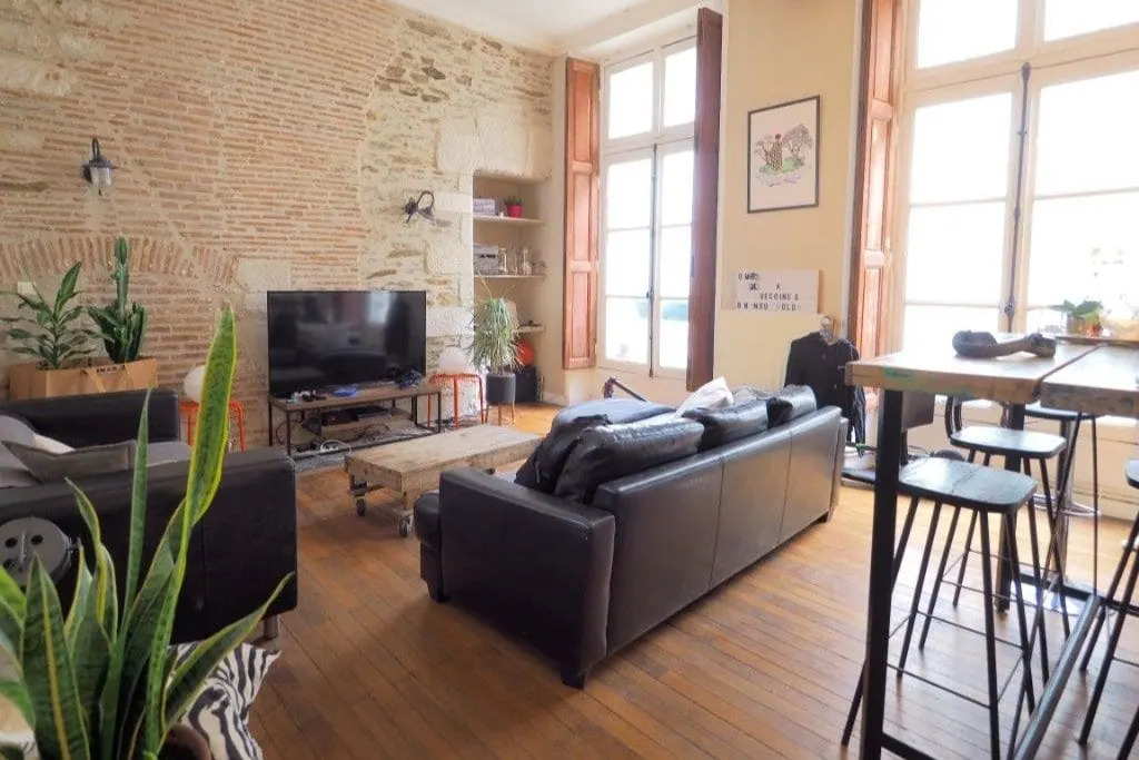 Salon lumineux d'un appartement ancien avec murs en pierre apparente et grandes fenêtres
