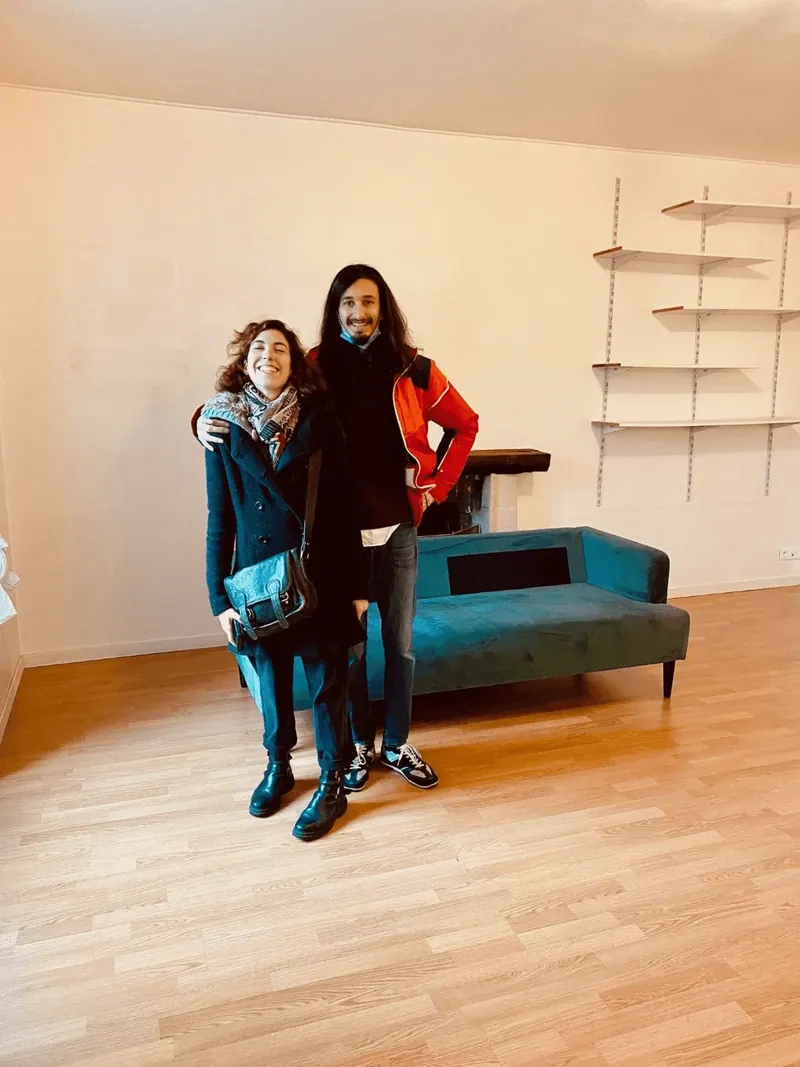 Un couple de clients posant dans son nouvel appartement, devant un canapé turquoise
